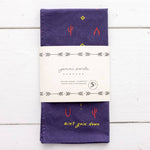 The Heritage Cotton Bandana - “Ain’T Goin’ Down” by Jenni Earle is a folded purple western bandana featuring small red and yellow designs, with the phrase “ain’t goin’ down” in yellow. It comes wrapped in a white paper label with Jenni Earle branding and product details—an ideal encouragement gift or a stylish cotton accessory for any occasion.