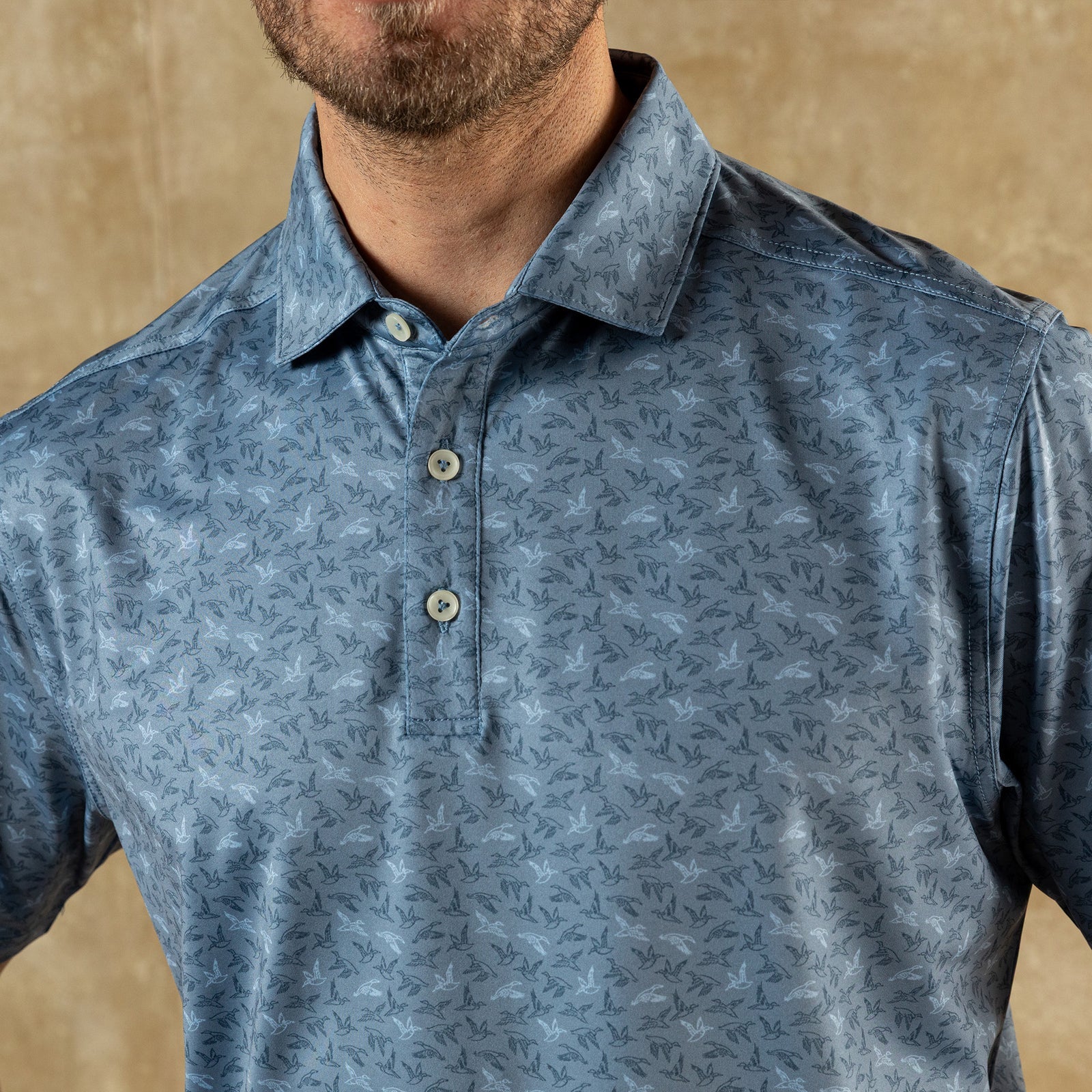 A man wearing the Duck Head Long Drive Performance Polo with a collar and three buttons stands against a neutral beige background.