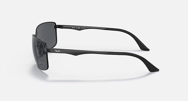 Side view of Ray-Ban 3498 sunglasses in black with rectangular lenses and slim, curved arms accented by brushed aluminum temples, set against a light grey background.