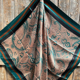 The Emerald and Tan Paisley Wild Rag by Rodeo Drive features green and brown paisley patterns with a striped border, elegantly draped on rustic wood for a classic western touch.