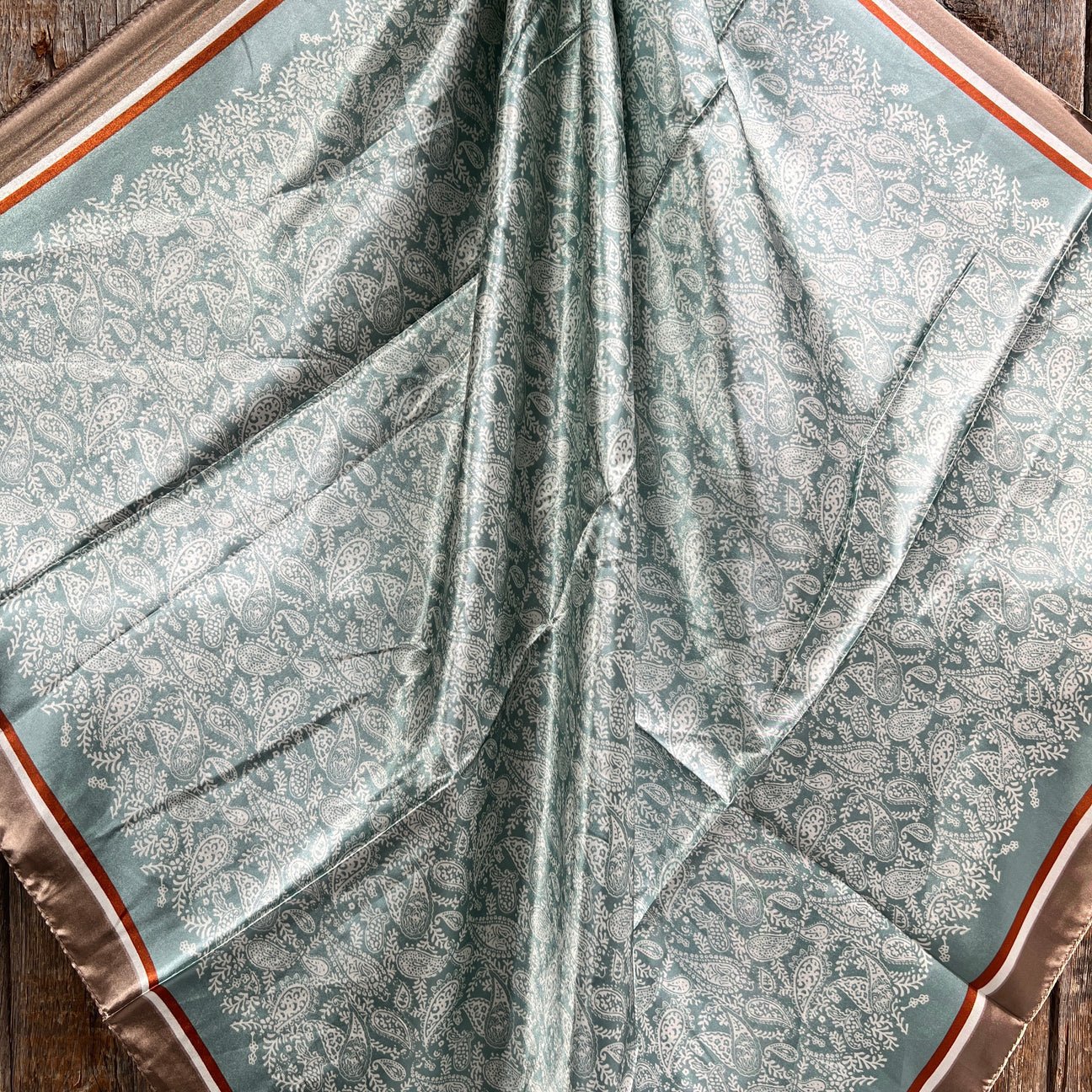 The Rodeo Drive Seafoam and Cream Paisley Wild Rag features intricate white floral motifs with brown and cream borders, perfect for adding western flair to any outfit.