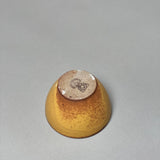 The Stoneware Smudge Bowl by Incausa is pictured upside down on a gray surface, highlighting the logo on its unglazed base.