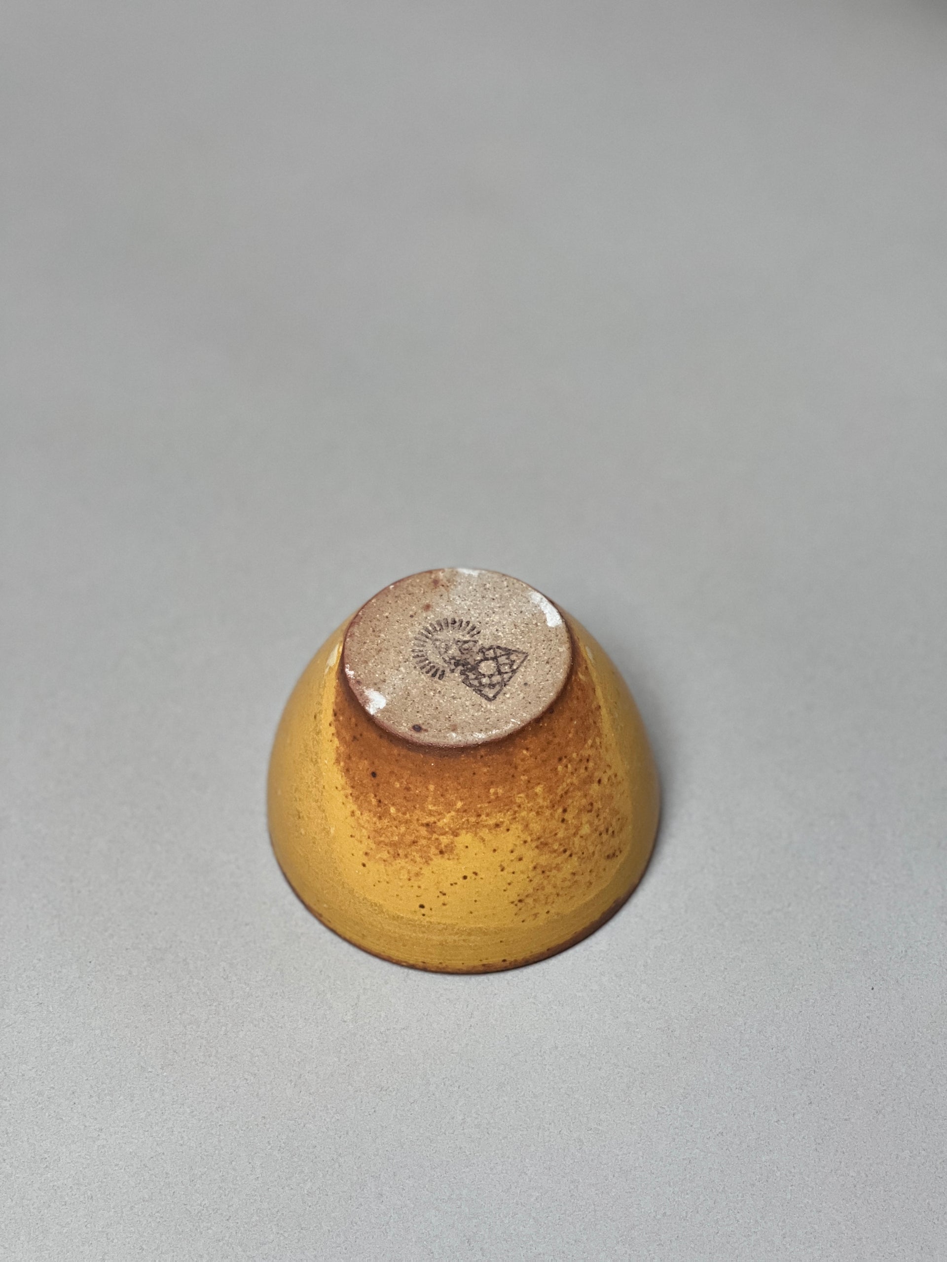 The Stoneware Smudge Bowl by Incausa is pictured upside down on a gray surface, highlighting the logo on its unglazed base.