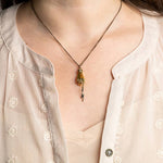 Magician’s Hand Necklace – Aged Brass Chain featuring an antique gold hand holding a small lightning bolt pendant on a thin chain.