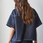 A person with long wavy brown hair wears the By Together Denim Embroidered short sleeve top and matching pants, standing with their back to the camera.