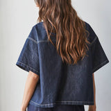 A person with long wavy brown hair wears the By Together Denim Embroidered short sleeve top and matching pants, standing with their back to the camera.