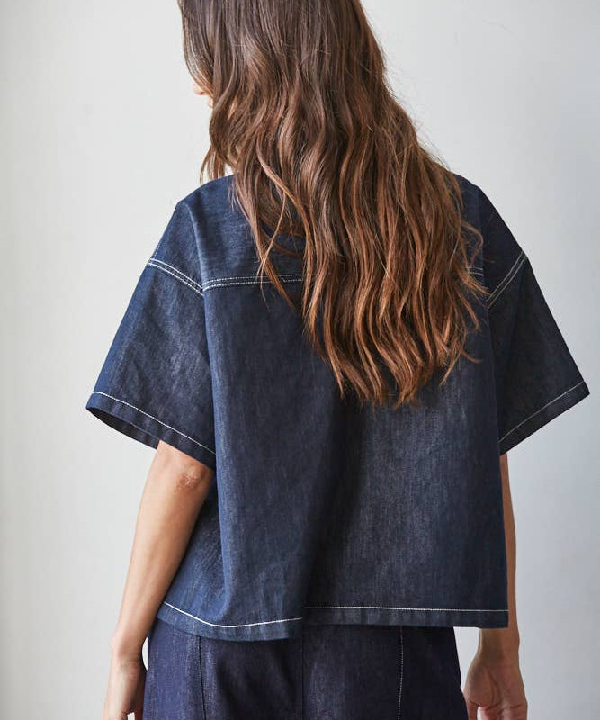 A person with long wavy brown hair wears the By Together Denim Embroidered short sleeve top and matching pants, standing with their back to the camera.