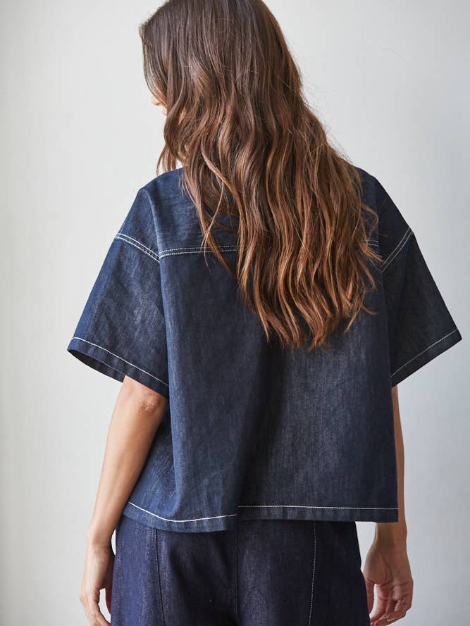 A person with long wavy brown hair wears the By Together Denim Embroidered short sleeve top and matching pants, standing with their back to the camera.