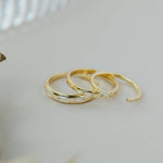 Three Gold Rings | Inset Baguette by JaxKelly are arranged in a row on a light surface, with part of a textured glass object visible in the background.
