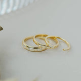 Three Gold Rings | Inset Baguette by JaxKelly are arranged in a row on a light surface, with part of a textured glass object visible in the background.