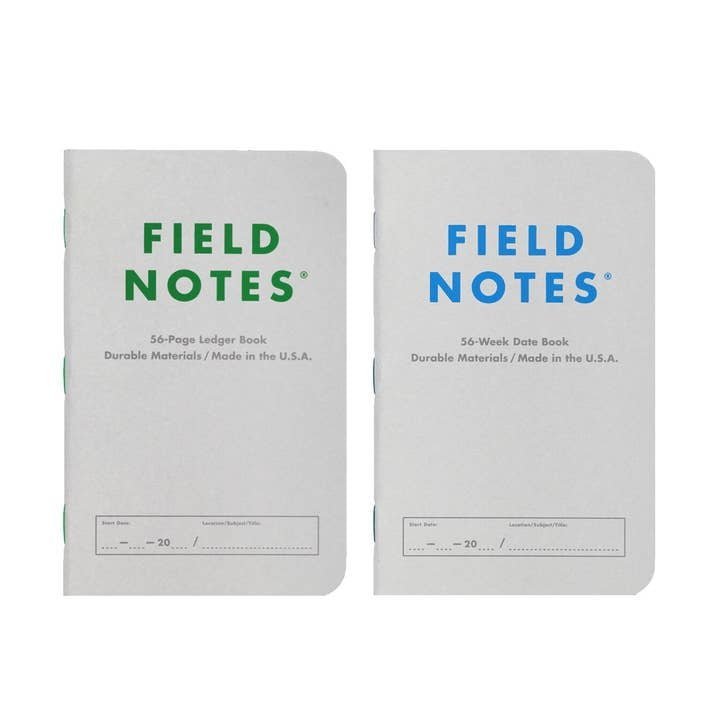 Two Field Notes memo books—one green-labeled "56-Page Ledger Book" and one blue-labeled "56-Week Date Book" from Field Notes—both with white covers and made in the U.S.A.; ideal for your next set of log books.