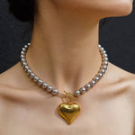 A Raissa Two Tone Heart Necklace featuring silver-toned beads, a gold-toned pendant, and a front toggle clasp, worn around a neck.
