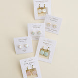 Six pairs of JaxKelly Gemstone Mini Drop earrings on display cards are arranged on a beige background, featuring mother of pearl, opal, amazonite, and Rose Quartz designs. These stylish and durable pieces from JaxKelly are tarnish-resistant—perfect for everyday wear.