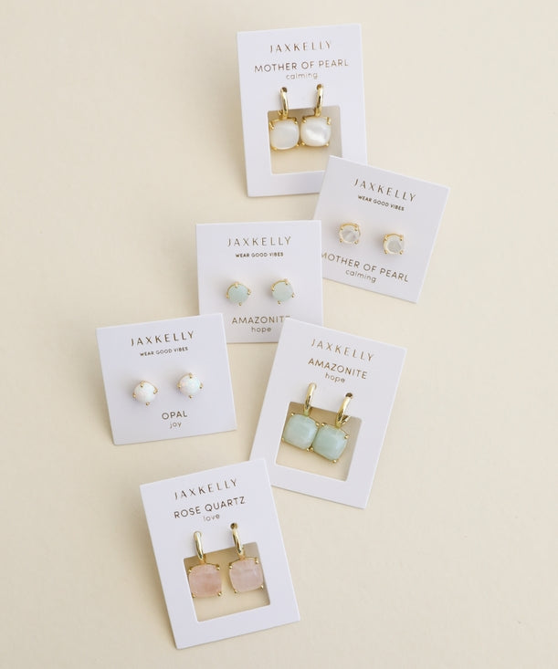 Six pairs of JaxKelly Gemstone Mini Drop earrings on display cards are arranged on a beige background, featuring mother of pearl, opal, amazonite, and Rose Quartz designs. These stylish and durable pieces from JaxKelly are tarnish-resistant—perfect for everyday wear.