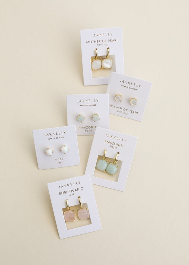 Six pairs of JaxKelly Gemstone Mini Drop earrings on display cards are arranged on a beige background, featuring mother of pearl, opal, amazonite, and Rose Quartz designs. These stylish and durable pieces from JaxKelly are tarnish-resistant—perfect for everyday wear.