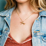 A gold Wild Horses Necklace featuring a horse charm pendant on a delicate cable chain worn around a person’s neck.