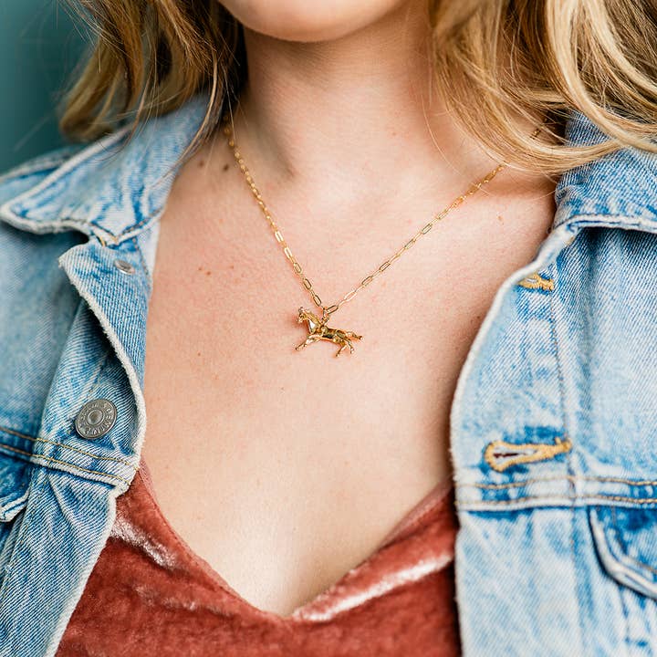 A gold Wild Horses Necklace featuring a horse charm pendant on a delicate cable chain worn around a person’s neck.