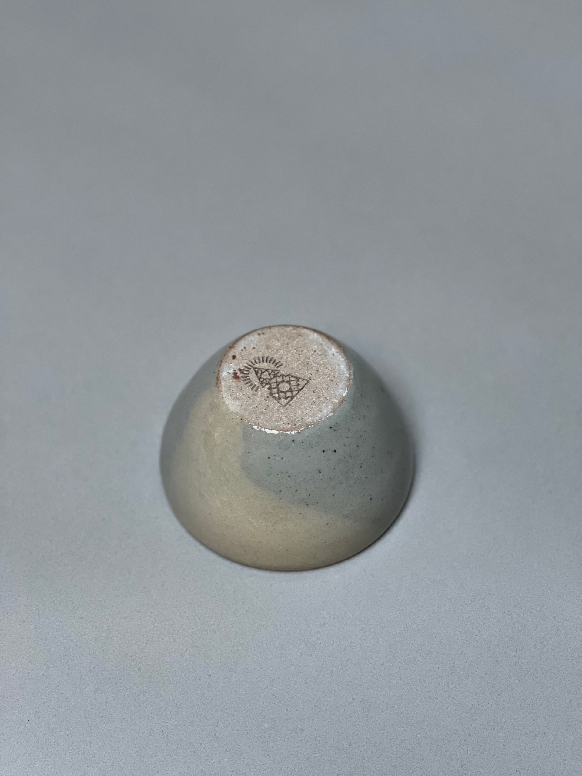 The Stoneware Smudge Bowl by Incausa is a small, hand-thrown ceramic piece with a glossy gray gradient glaze and stamped base, shown upside-down on a plain, light gray surface.