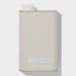 A beige rectangular metal container labeled “Signature Cozy | Mozi” by Mozi, featuring a white cap on top and casting a shadow to the right. This laundry detergent provides a subtle honey fragrance for a refreshing laundry experience.