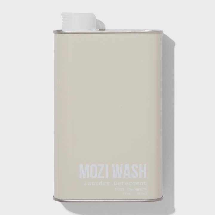 A beige rectangular metal container labeled “Signature Cozy | Mozi” by Mozi, featuring a white cap on top and casting a shadow to the right. This laundry detergent provides a subtle honey fragrance for a refreshing laundry experience.