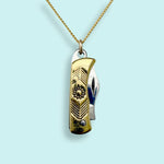 The Gold Wildflower Knife Necklace by Ornamental Things features a functional gold and silver knife pendant suspended from a gold chain, displayed against a light blue background.