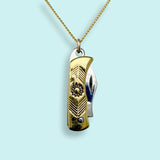 The Gold Wildflower Knife Necklace by Ornamental Things features a functional gold and silver knife pendant suspended from a gold chain, displayed against a light blue background.