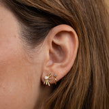 Close-up of a person's ear wearing JaxKelly's Sun Ray - White Opal - Gold Earrings, featuring lab-grown white opal and 18k gold plating, alongside a small gold hoop with a tiny gemstone.