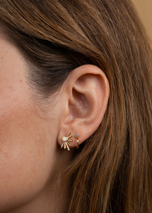 Close-up of a person's ear wearing JaxKelly's Sun Ray - White Opal - Gold Earrings, featuring lab-grown white opal and 18k gold plating, alongside a small gold hoop with a tiny gemstone.