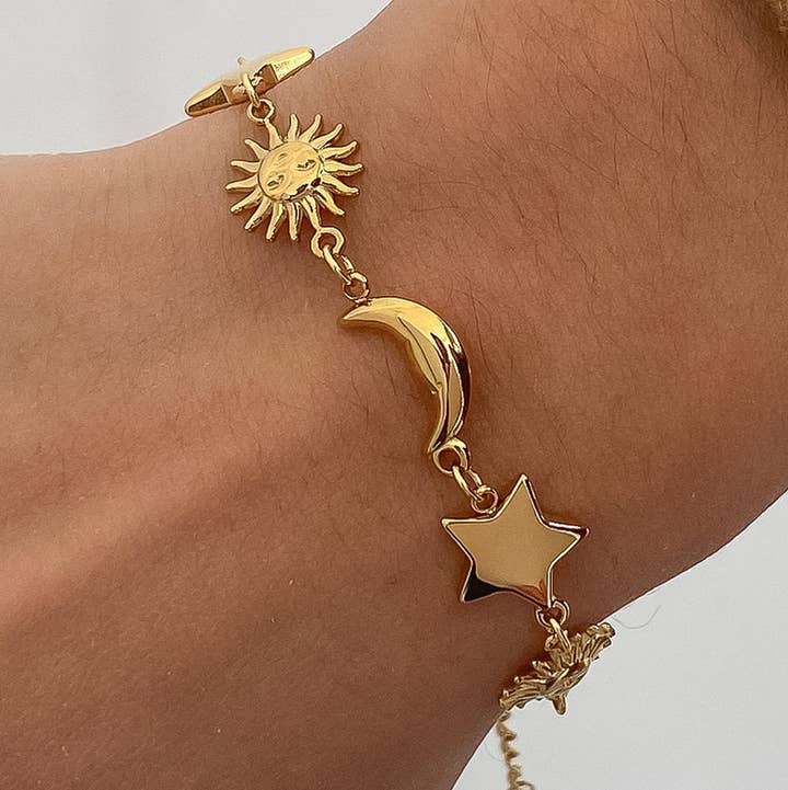 Leonora Sun and Star Bracelet by Flanerie by MAIQ, a non-tarnish 18K gold bracelet featuring sun, crescent moon, and star charms worn on a wrist.