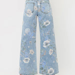 A person is shown from the back against a plain white background, wearing the Vervet Super High Rise Floral Extreme Vintage Flare Jeans in light blue with a wide-leg silhouette and white heeled shoes.