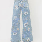 A person is shown from the back against a plain white background, wearing the Vervet Super High Rise Floral Extreme Vintage Flare Jeans in light blue with a wide-leg silhouette and white heeled shoes.