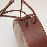 Close-up of the Joi Bag by Stash, showcasing Japanese-inspired design with brown leather accents, braided leather handles, beige sand roughout suede sides, and a small metal button detail.