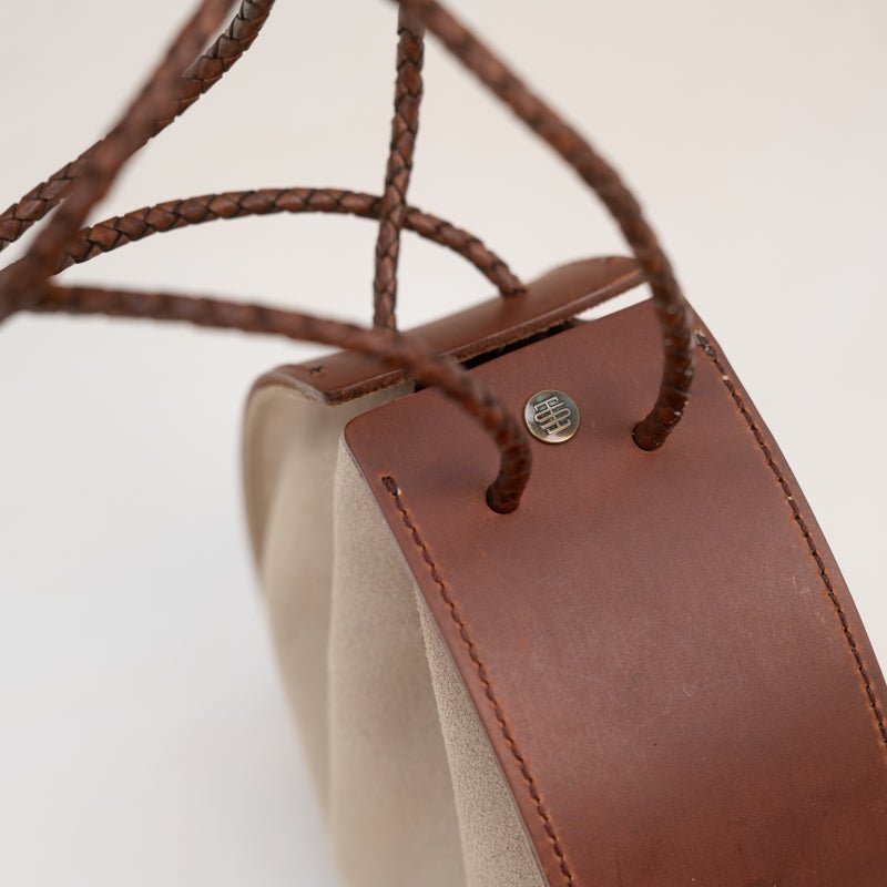 Close-up of the Joi Bag by Stash, showcasing Japanese-inspired design with brown leather accents, braided leather handles, beige sand roughout suede sides, and a small metal button detail.