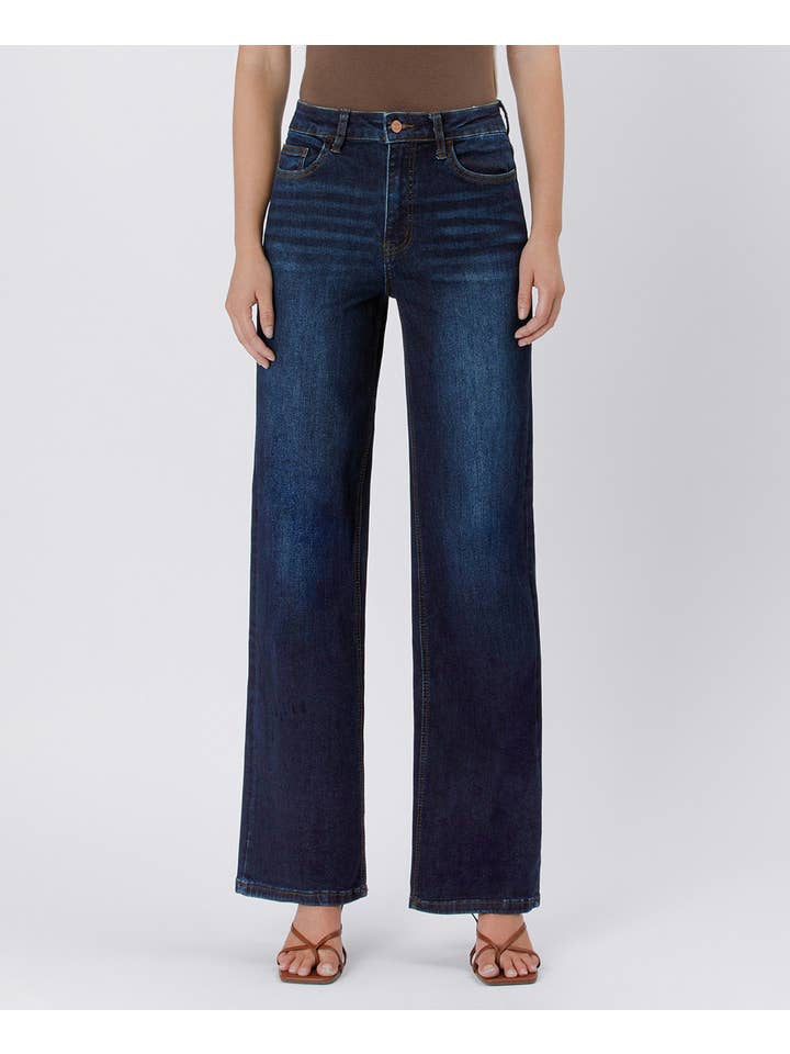 A person models Vervet's 90's Vintage Super High Rise Dark Wash Loose Jeans with a brown top and matching sandals, standing against a plain light background.