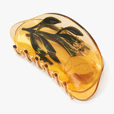 The Buttercup Wild Flower Claw by Winona Irene is an amber-colored hair accessory crafted from cellulose acetate, featuring a raised yellow flower and green leaves encased in the design—perfect for any occasion.