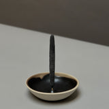An incense stick stands upright in the Incausa Stoneware Holder, featuring a black interior and beige exterior, crafted by Incausa and placed on a flat surface.