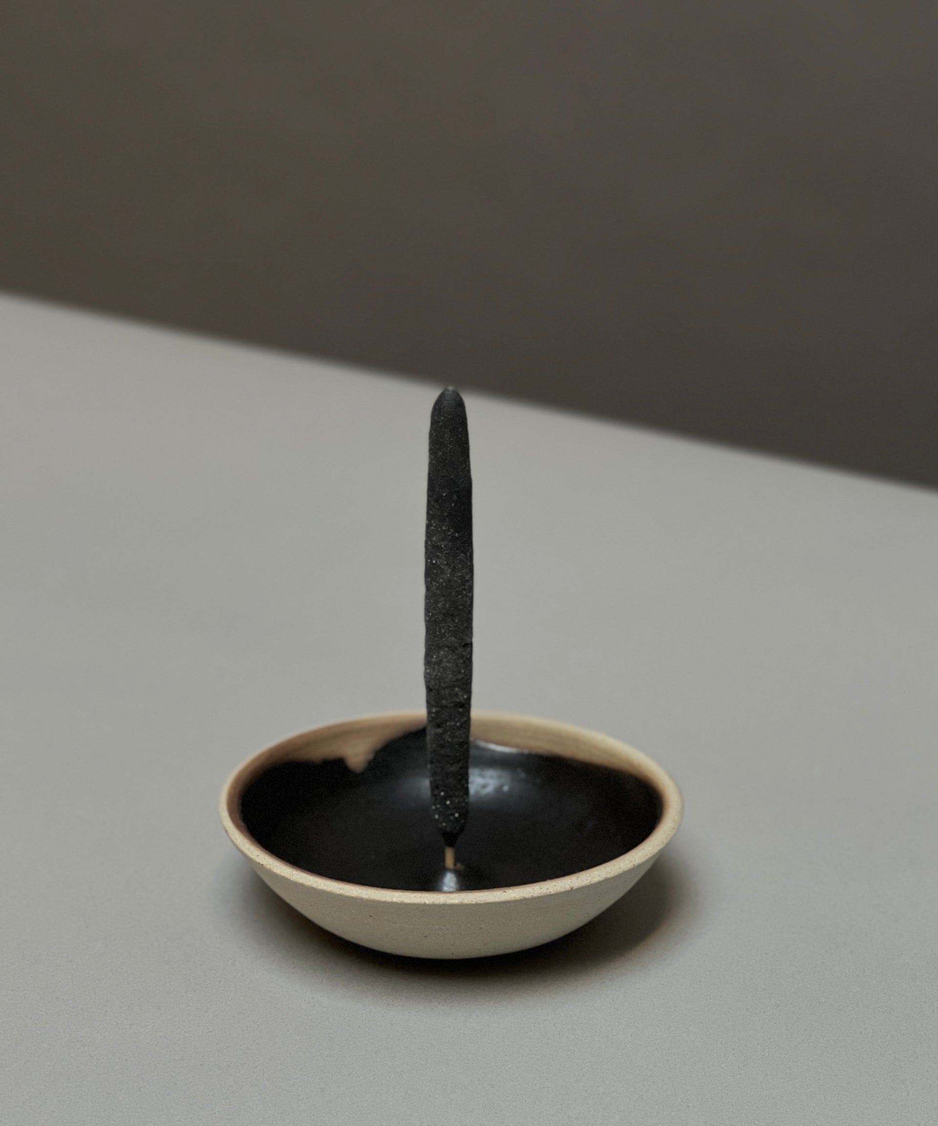 An incense stick stands upright in the Incausa Stoneware Holder, featuring a black interior and beige exterior, crafted by Incausa and placed on a flat surface.