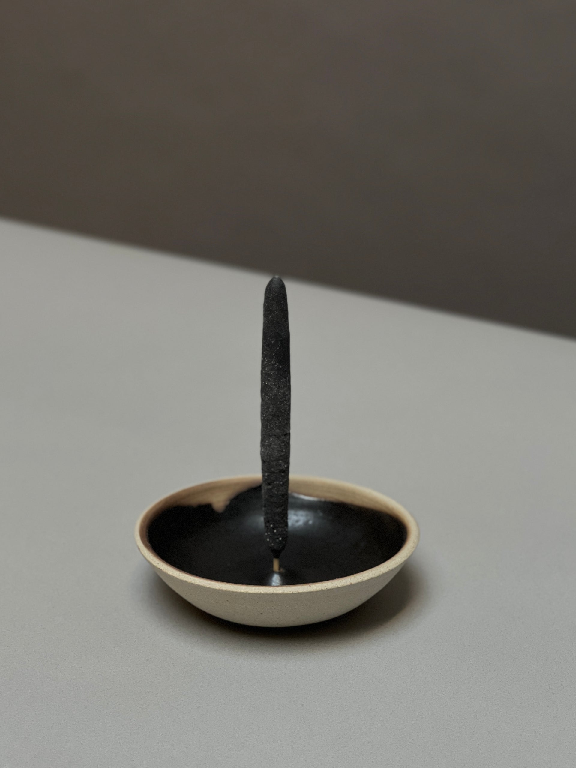 An incense stick stands upright in the Incausa Stoneware Holder, featuring a black interior and beige exterior, crafted by Incausa and placed on a flat surface.