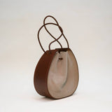 Introducing the Joi Bag by Stash in Sand Roughout—a compact, round Japanese-inspired accessory featuring a beige fabric center and brown braided handles, elegantly showcased against a simple light background.