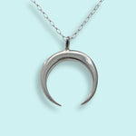 The Sterling Silver Crescent Moon Necklace by Ornamental Things features a crescent moon pendant crafted from sterling silver, hanging from a delicate, nickel-free chain and displayed against a light blue background.