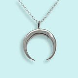 The Sterling Silver Crescent Moon Necklace by Ornamental Things features a crescent moon pendant crafted from sterling silver, hanging from a delicate, nickel-free chain and displayed against a light blue background.