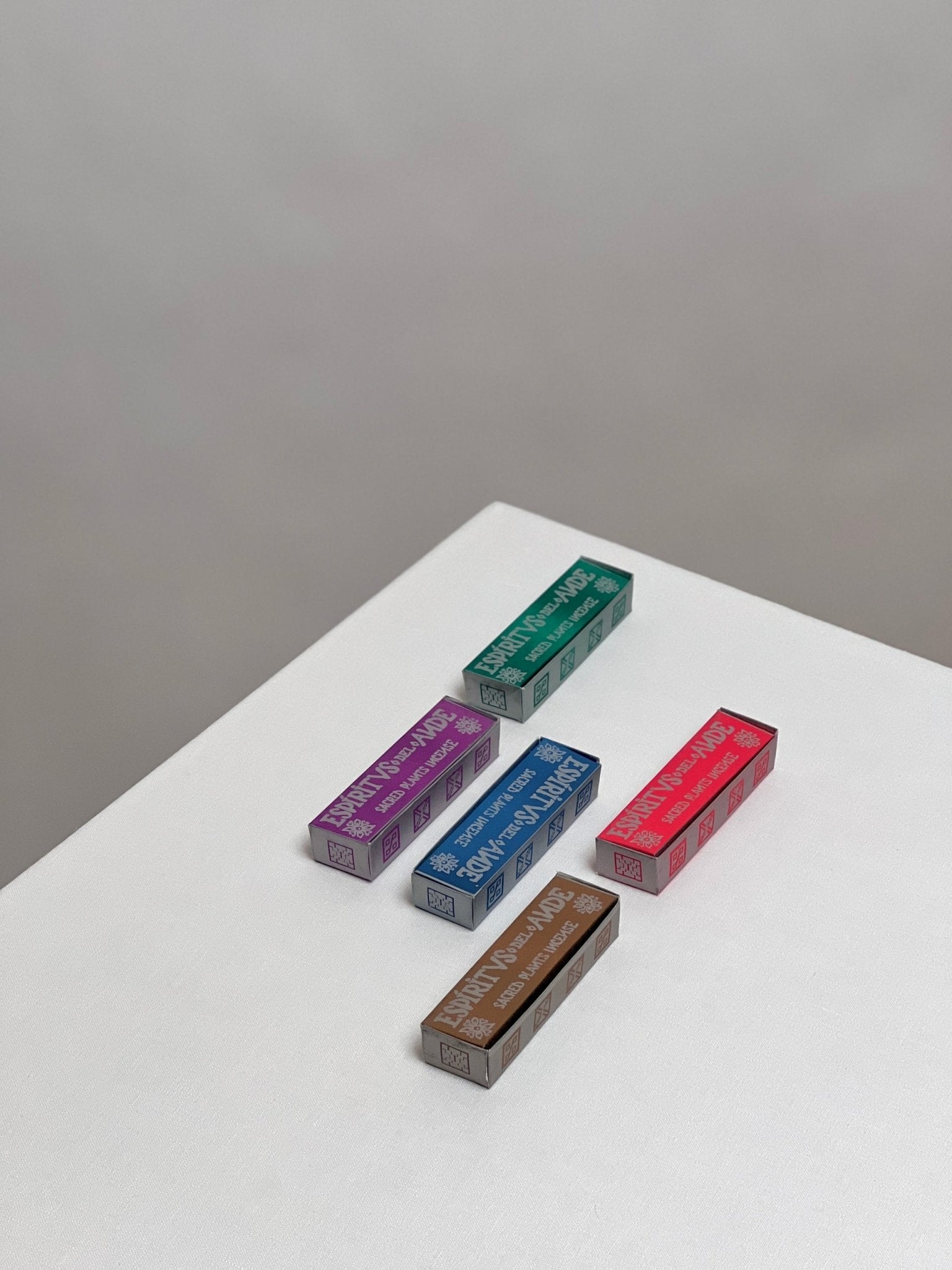 Five colorful rectangular boxes from the Espiritus del Ande Collection by Incausa are arranged on a white surface, each featuring unique designs inspired by natural incense and Palo Santo blends handcrafted in Peru.
