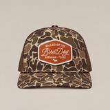 The Badge Hat by Ballad Originals is a camouflage trucker cap featuring a mesh back and an orange-and-white patch emblazoned with “Ballad of the Bird Dog, Brenham, Texas” on the front. Combining classic Western style with breathable comfort, it’s perfect for everyday wear.