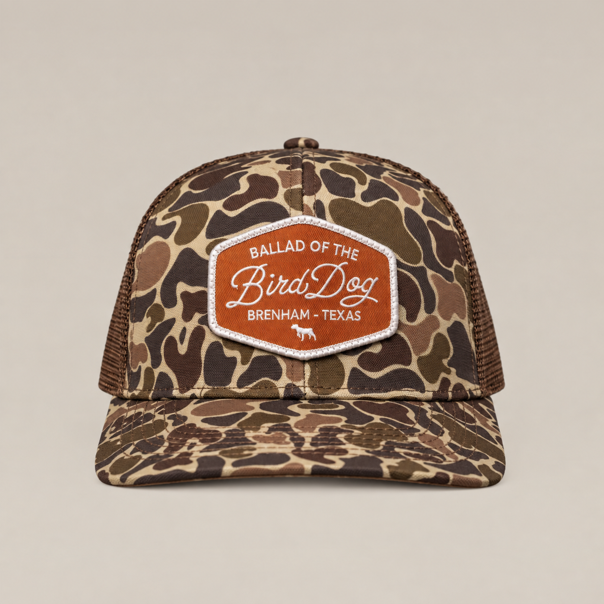 The Badge Hat by Ballad Originals is a camouflage trucker cap featuring a mesh back and an orange-and-white patch emblazoned with “Ballad of the Bird Dog, Brenham, Texas” on the front. Combining classic Western style with breathable comfort, it’s perfect for everyday wear.