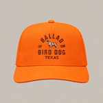 The Field Companion Hat - Ballad Originals by Ballad of the Bird Dog is a bright orange trucker hat with a mesh back, showcasing black embroidered “Ballad of the Bird Dog Texas” text and a small dog graphic on the front for a blend of classic Western style and modern comfort.