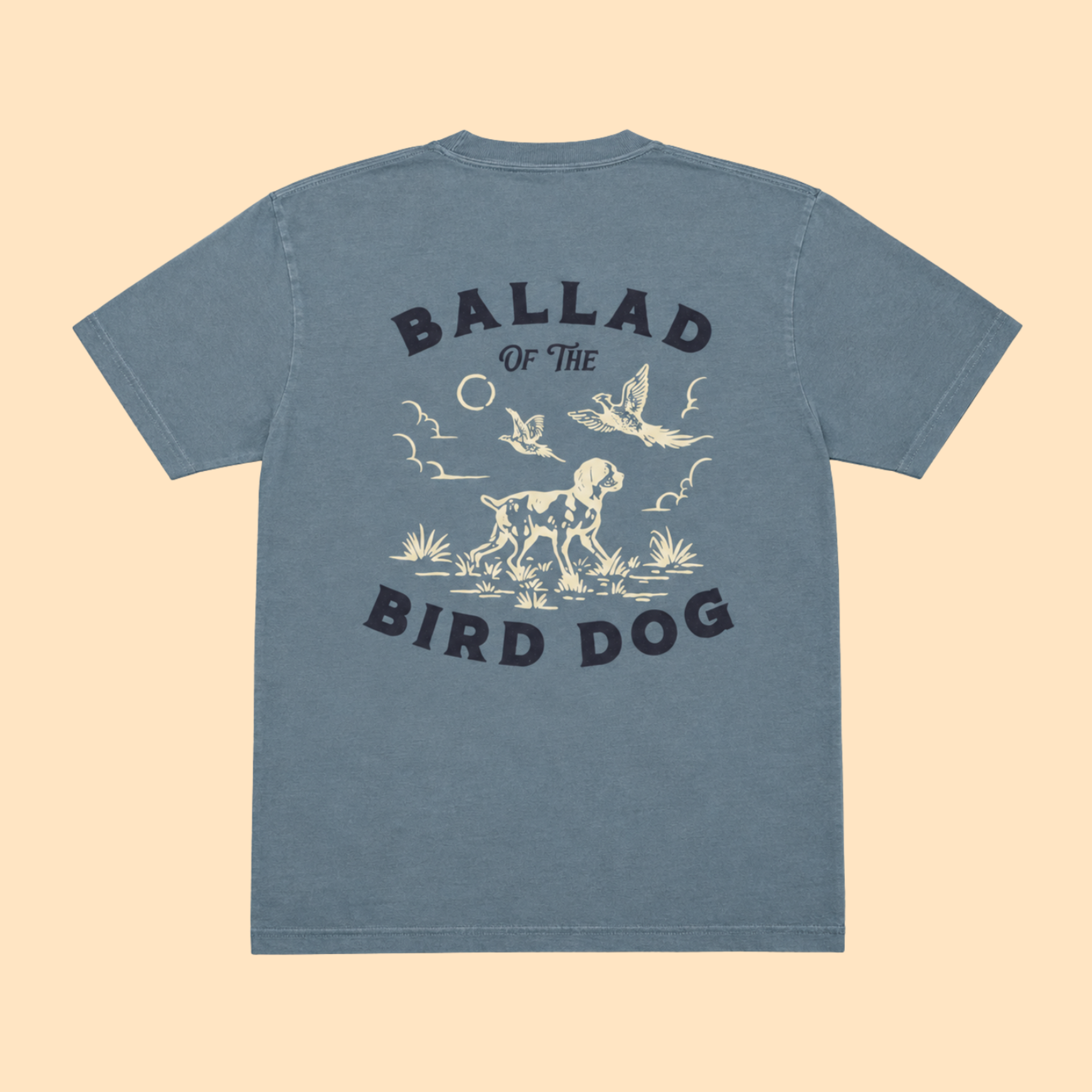 Introducing the Pheasant Flush Shirt - Ballad Originals by Ballad of the Bird Dog. This blue t-shirt features a cream and black graphic depicting a dog, birds, and plants inspired by classic upland bird hunting scenes. The phrase “Ballad of the Bird Dog” is printed on the back, making it a standout choice for any pheasant hunting shirt collection.