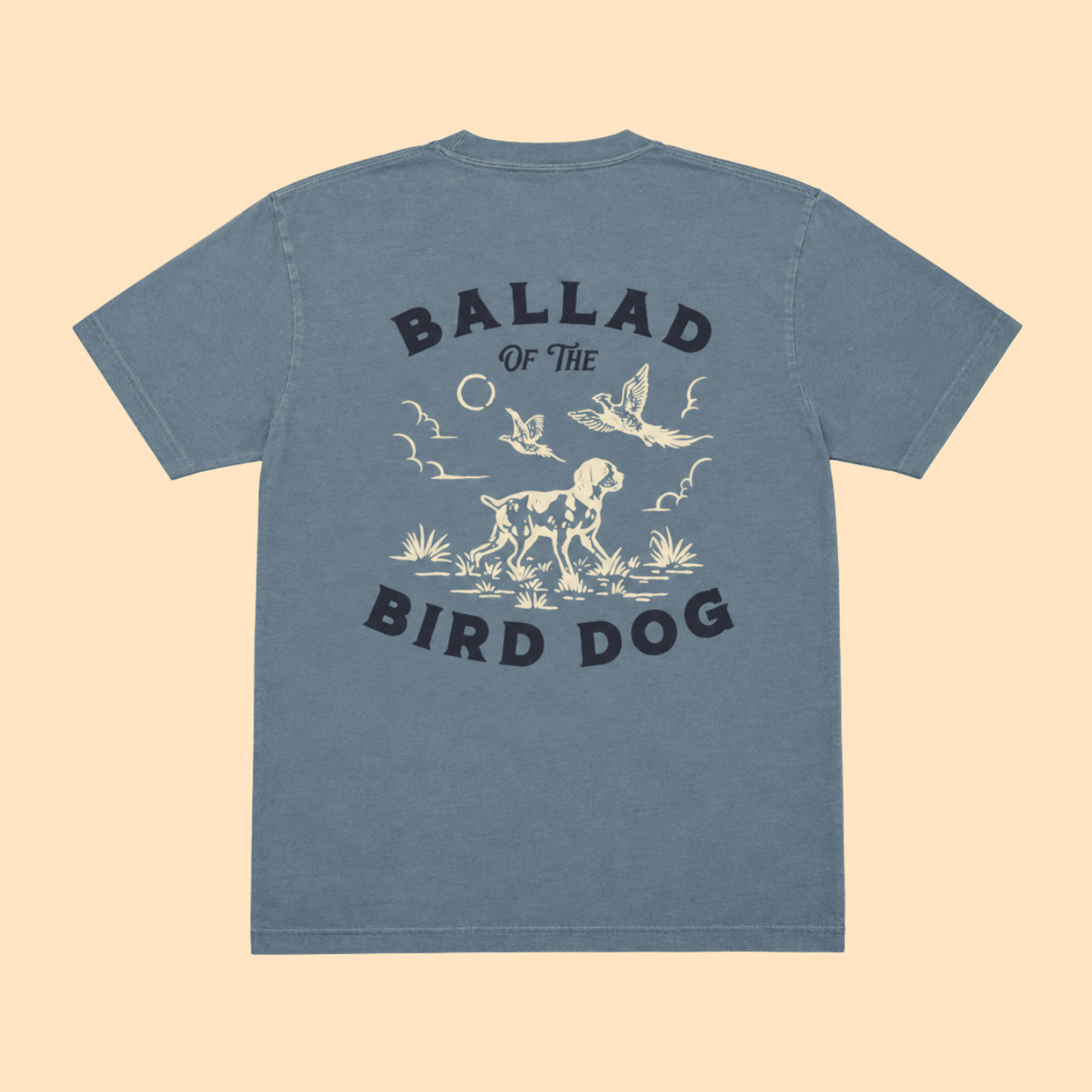 Introducing the Pheasant Flush Shirt - Ballad Originals by Ballad of the Bird Dog. This blue t-shirt features a cream and black graphic depicting a dog, birds, and plants inspired by classic upland bird hunting scenes. The phrase “Ballad of the Bird Dog” is printed on the back, making it a standout choice for any pheasant hunting shirt collection.