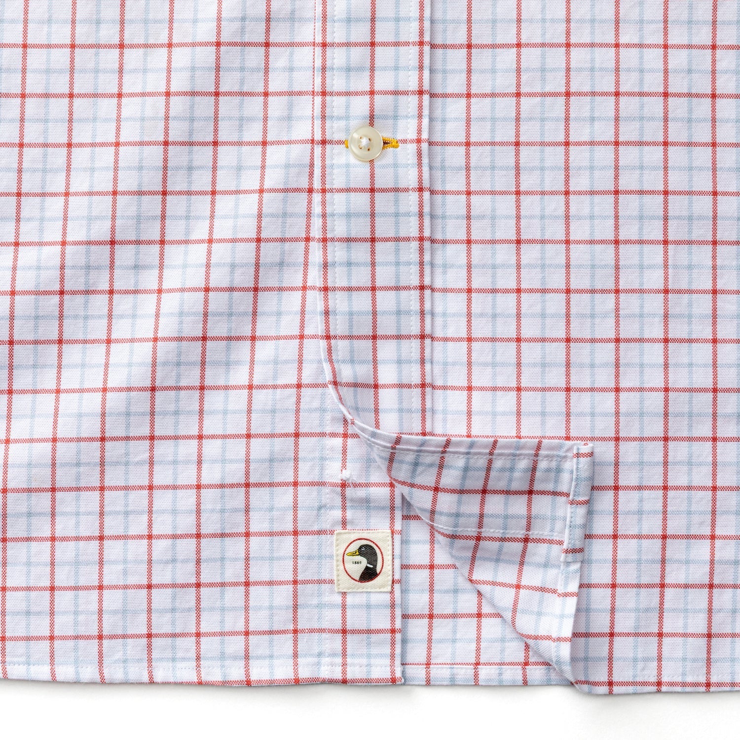 Close-up of a Duck Head Cotton Oxford Sport Shirt in white with red grid pattern, featuring button details and a small person illustration on the inner placket.