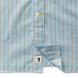 A close-up of the Duck Head Cotton Cashmere Poplin Sport Shirt in blue plaid with tan and white lines, featuring a white button and a small toucan logo tag near the bottom hem.