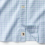 A close-up of the Cotton Twill Sport Shirt by Duck Head in light blue and green plaid, featuring buttons, a pocket, and a small square tag with a black duck graphic near the bottom hem.